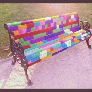 A colorful yarn bomb on a park bench.